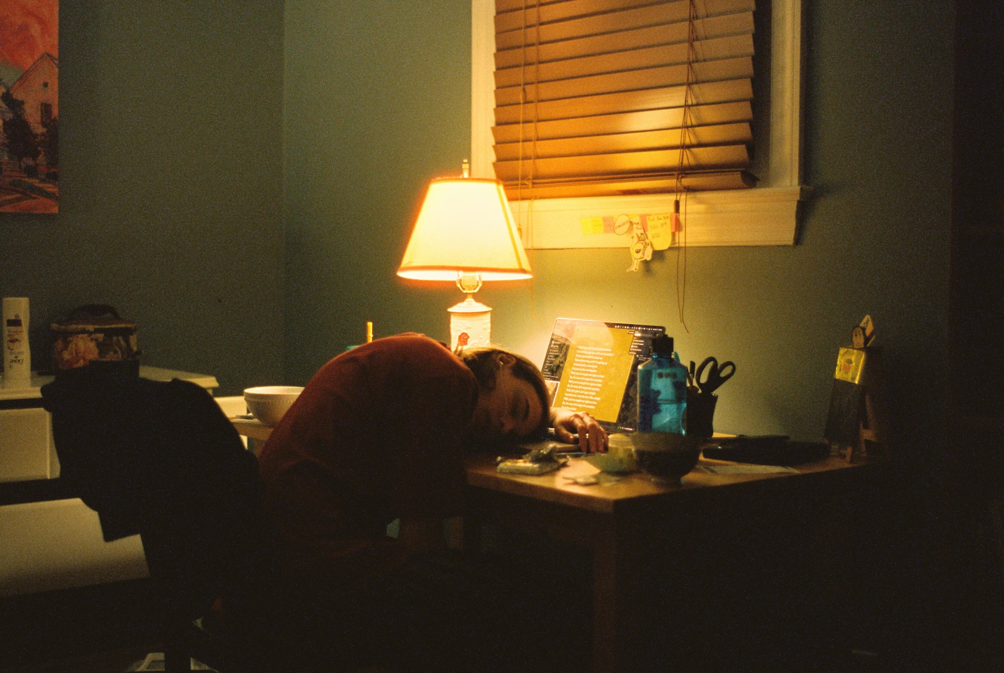 A student asleep at a desk under a lamp
